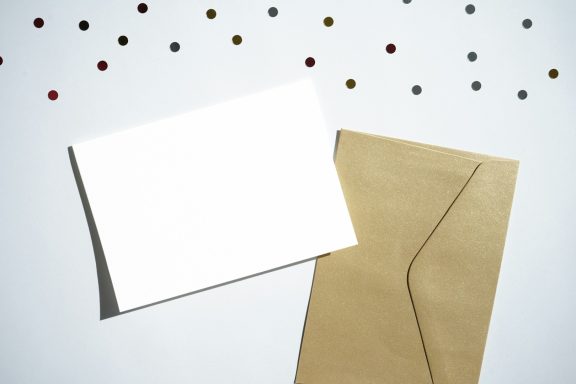 Blank white card next to a brown envelope, surrounded by colourful confetti.
