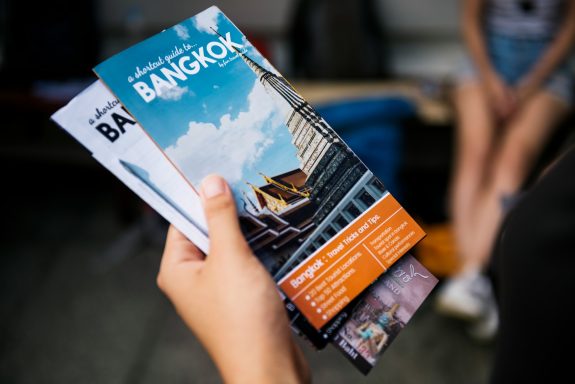 A hand holding a Bangkok travel brochure with images and text.